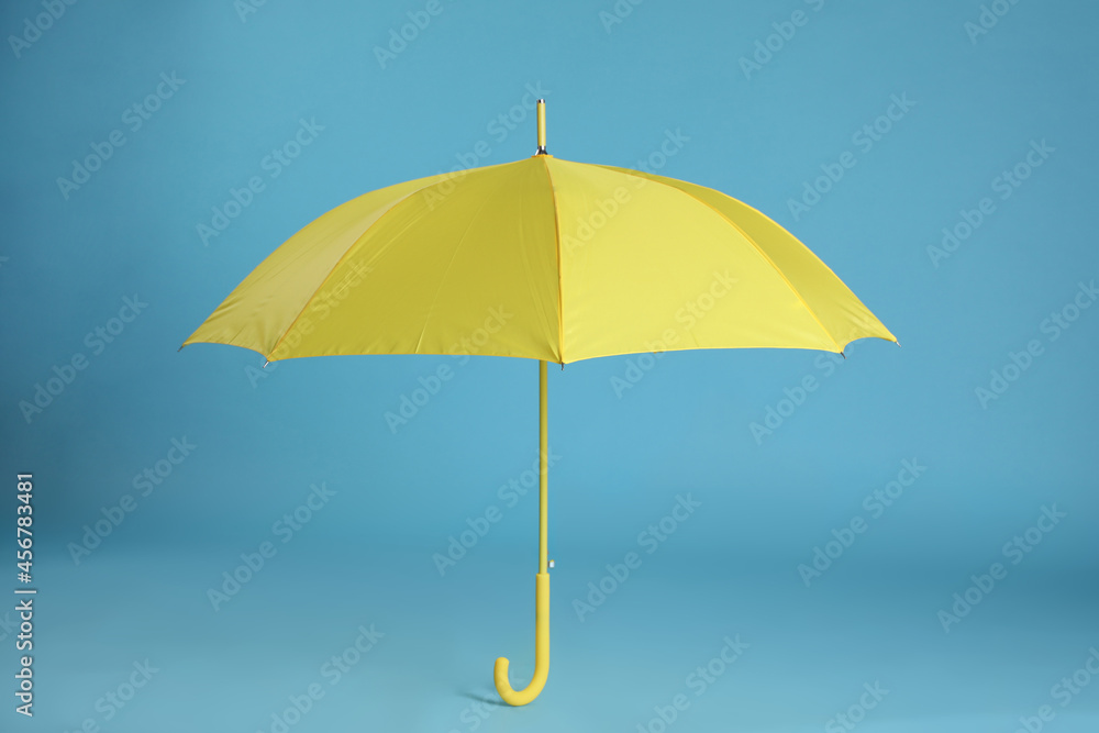 Stylish open yellow umbrella on light blue background