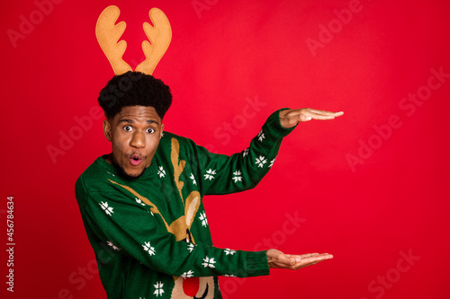 Portrait of attractive amazed cheerful guy wearing deer horns showing copy space size object isolated over bright red color background