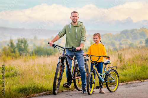 Happy father and daughter take bike ride in nature in autumn.