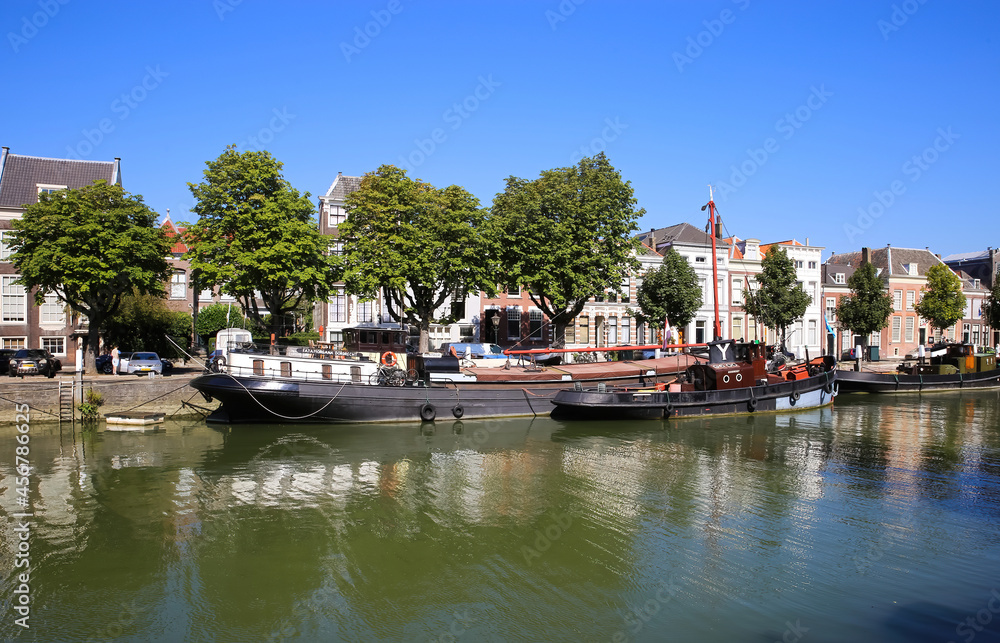 Dordrecht, Netherlands - July 9. 2021: View on typical inland water canal harbor with old sail ship against blue summer sky