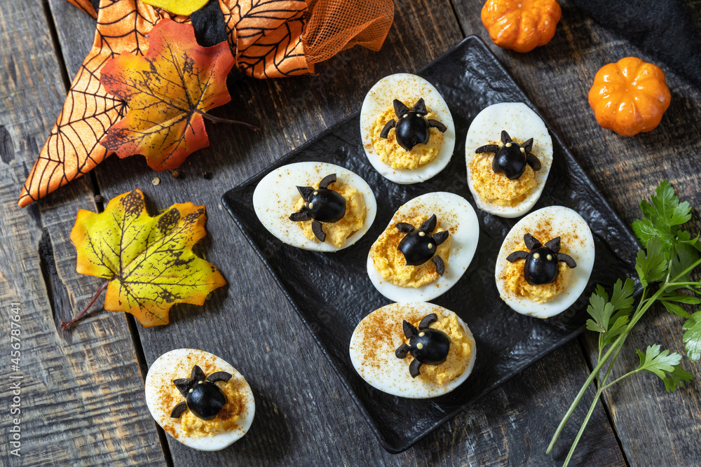 Halloween funny idea for party food. Halloween creative set stuffed eggs with paprica and bat on a wooden table. Halloween funny idea for party food. Halloween creative set stuffed eggs with paprica and bat on a wooden table.
