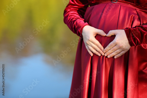 Banner with female hands in the form of a heart on the background of the belly - a symbol of love for the unborn child. Pregnant woman. Maternity concept.