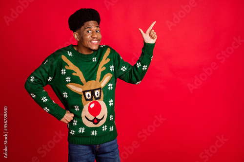 Portrait of attractive cheerful guy wearing ugly jumper demonstrating copy space ad offer isolated over bright red color background