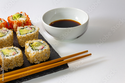 Gourmet sushi tray on slate surface on white background with soy sauce and chopsticks. Copy space. Selective focus.