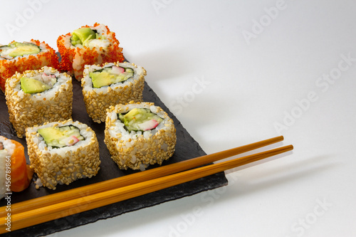 Gourmet sushi tray on slate surface on white background with chopsticks. Copy space. Selective focus.