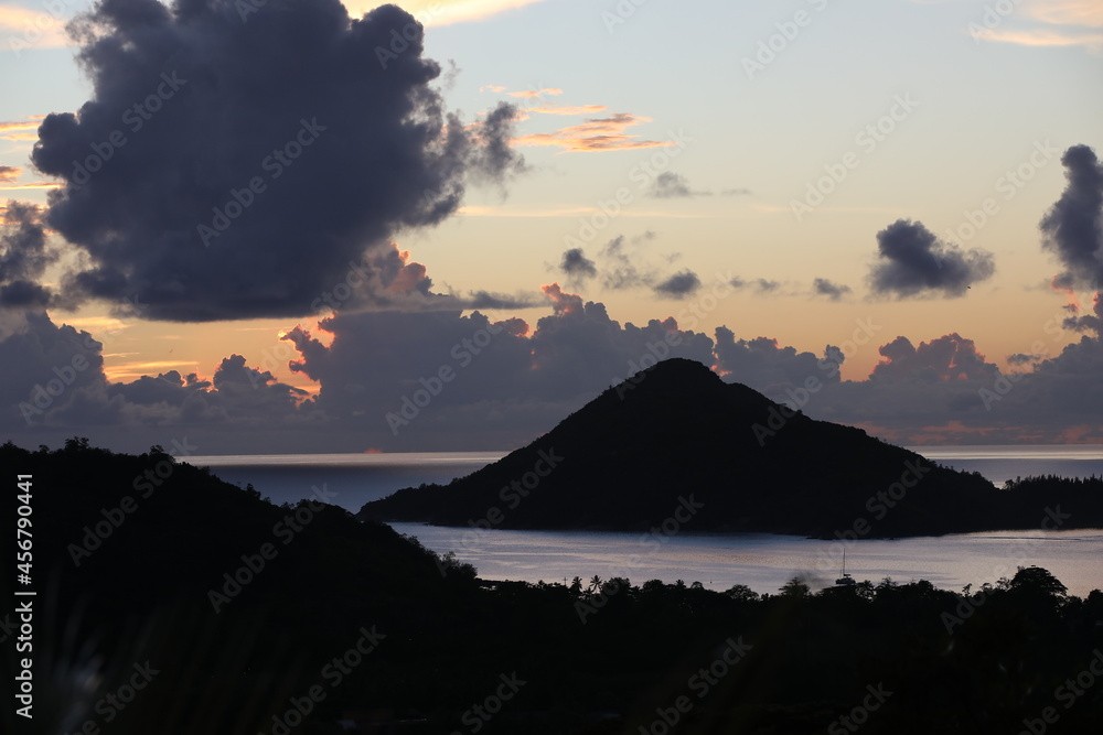 Sunset in the mountains above the sea with an island with gray clouds in the backlit sky on the horizon.