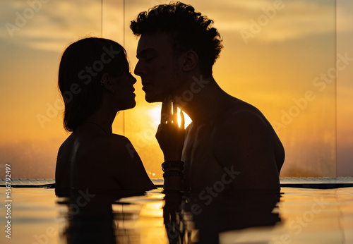 Silhouette of Loving couple in the infinity pole water during sunset. Romance and relationship