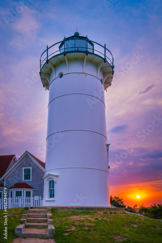 Sunrise behind the tall white Nobska Light with partial view of Lighthouse Keeper's House on the green hill in Woods Hole, Massachusetts.