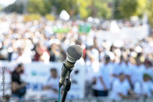 Focus on microphone, blurred group of people at mass protest or public demonstration in the background © wellphoto
