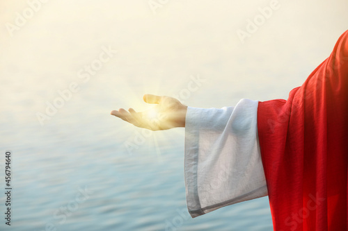 Jesus Christ near water outdoors, closeup. Miraculous light in hand
