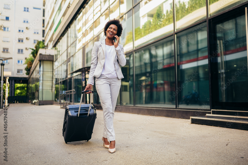 Full length portrait of excited young business woman using smart phone with travel bag