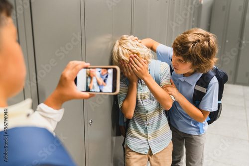 Schoolchildren cruel boys filming on the phone torturing bullying their classmate in school hall. Puberty difficult age photo