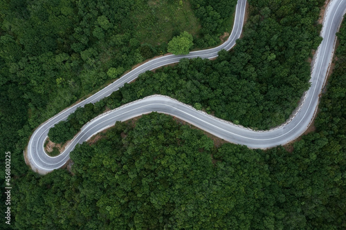 Aerial view of an empty winding road going through an area densely overgrown with green trees
