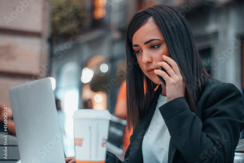 Asesora realizando una llamada telefónica con su telefono móvil a un cliente para comentar diversos asuntos sobre su trabajo en una cafeteria por la mañana tomando café y mirando el portátil