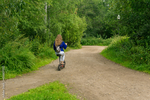 young woman rides an electric scooter along the path in the park