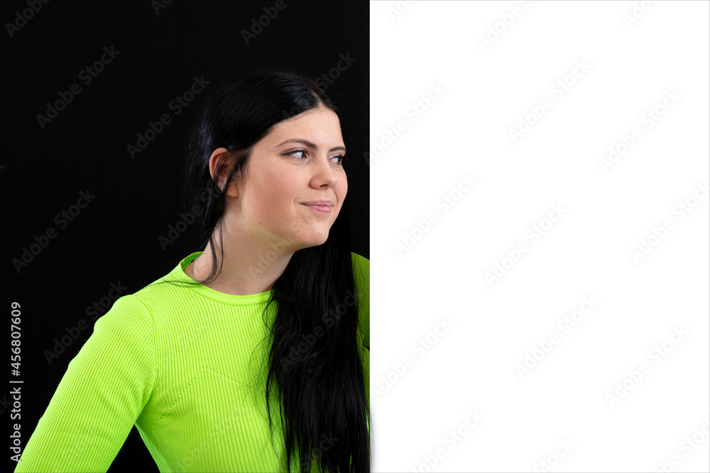 attractive dark-haired woman in bright colored clothes with a white blank poster, isolated on a dark attractive dark-haired woman in bright colored clothes with a white blank poster, isolated on a dark