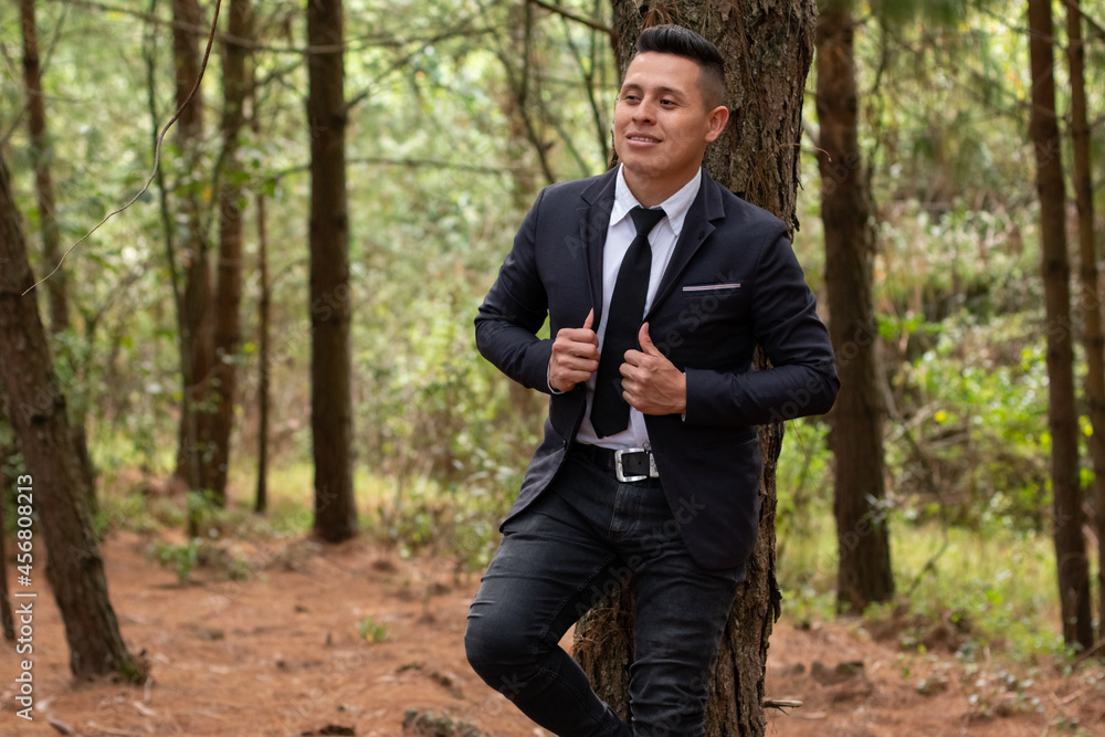 Latin man against a tree, wearing a suit and tie. Lush and colorful forest. Latin man against a tree, wearing a suit and tie. Lush and colorful forest.