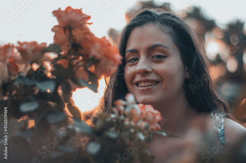 Mujer joven de vestido riendo con alegría en la naturaleza junto a las flores rosas y la puesta de sol del amanecer