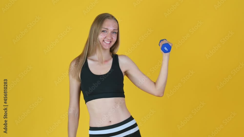 Portrait of attractive fitness woman holding dumbbell showing thumbs up gesture on yellow studio background Portrait of attractive fitness woman holding dumbbell showing thumbs up gesture on yellow studio background