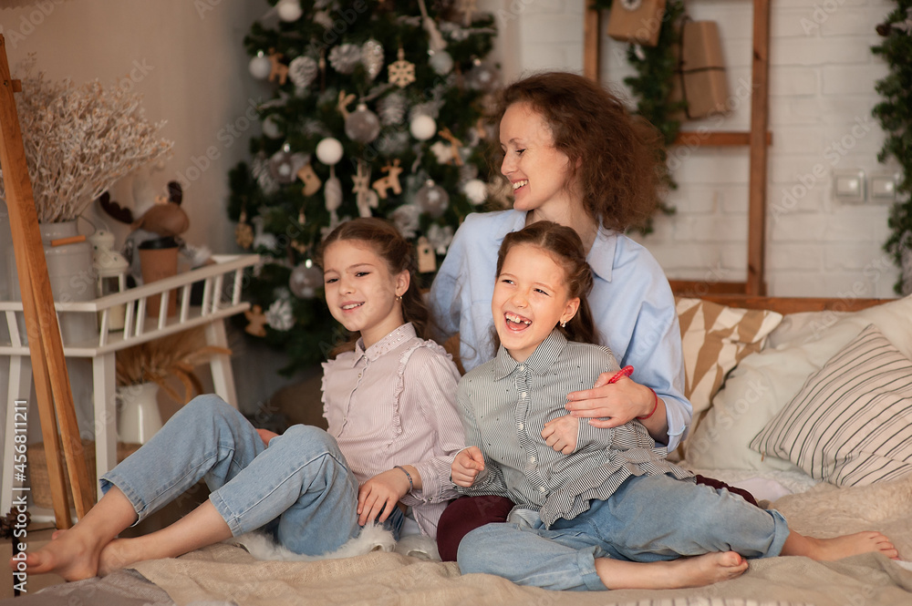 Mom and two daughters lie on a bed in a christmas bedroom interior