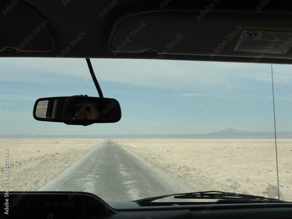 Driving a car on a road in Atacama Desert, Chile, during a sunny day. Showing the interior of the vehicle and the landscape outside: the road, sand, mountains and sky. Driving a car on a road in Atacama Desert, Chile, during a sunny day. Showing the interior of the vehicle and the landscape outside: the road, sand, mountains and sky.