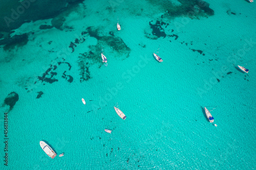 Aerial view of many yachts and sailboats in turquoise water in Mediterranean Sea next to Sardinia island, La Pelosa beach