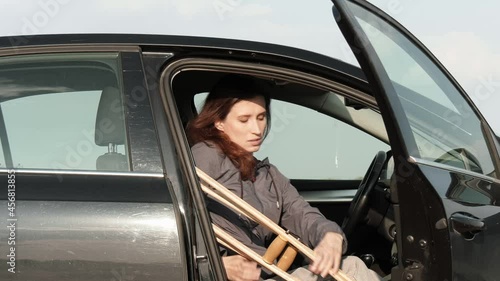 Disabled woman with a broken leg on crutches gets out of the car.