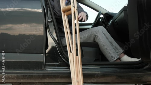 Disabled woman with a broken leg on crutches gets out of the car.