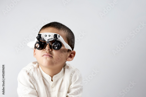 Studio portrait of little scientist in special magnifying headset glasses with copy space