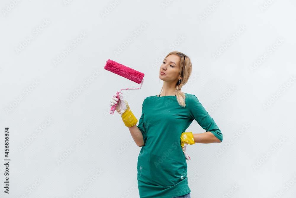 A young girl poses with a pink roller before painting a white wall. Repair of the interior. A young girl poses with a pink roller before painting a white wall. Repair of the interior.