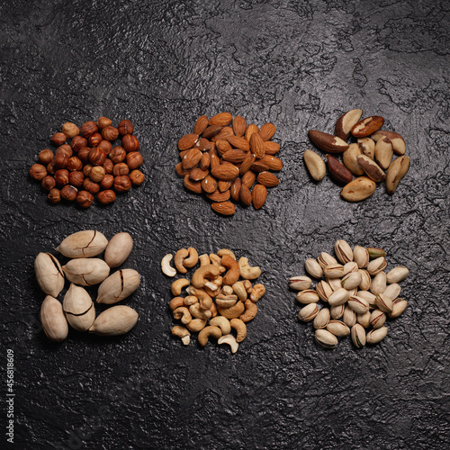 Piles of assorted nuts like pistachio, cashew, almond, hazelnut, Brazilian nut and pecan placed in even rows on black background 