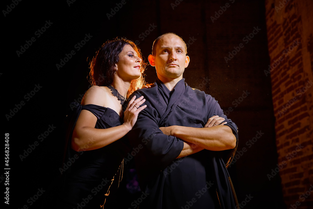 A couple in old dark clothes in an abandoned castle with old brick walls. A man and a woman posing in a dark gloomy mysterious dangerous hall. The evil king and Queen on Halloween