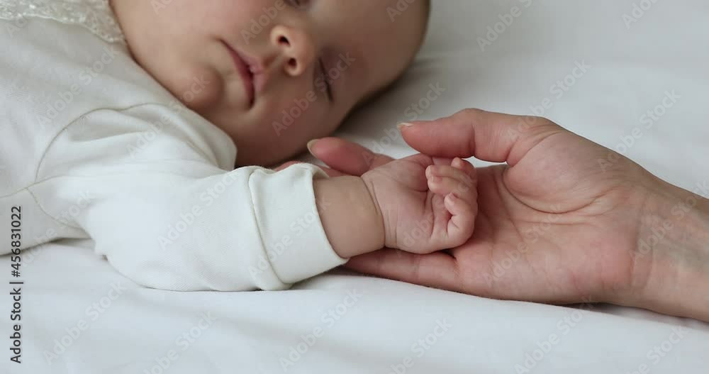 Close up view sweet newborn sleeping on bed, loving caring mother is near holding her baby hand, protect serene day nap. Healthy rest for growth and renew energy of children, carefree babyhood concept Close up view sweet newborn sleeping on bed, loving caring mother is near holding her baby hand, protect serene day nap. Healthy rest for growth and renew energy of children, carefree babyhood concept