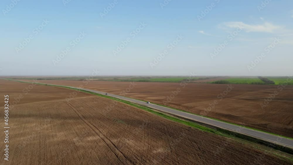 Grey long asphalt highway road with automobiles between brown ground fields under blue spring sky WITH clouds aerial view Grey long asphalt highway road with automobiles between brown ground fields under blue spring sky WITH clouds aerial view