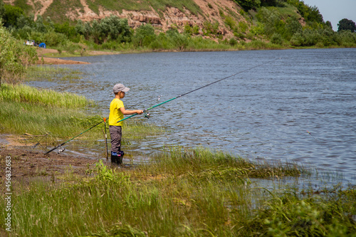 little fisherman with a fishing rod on the river bank
