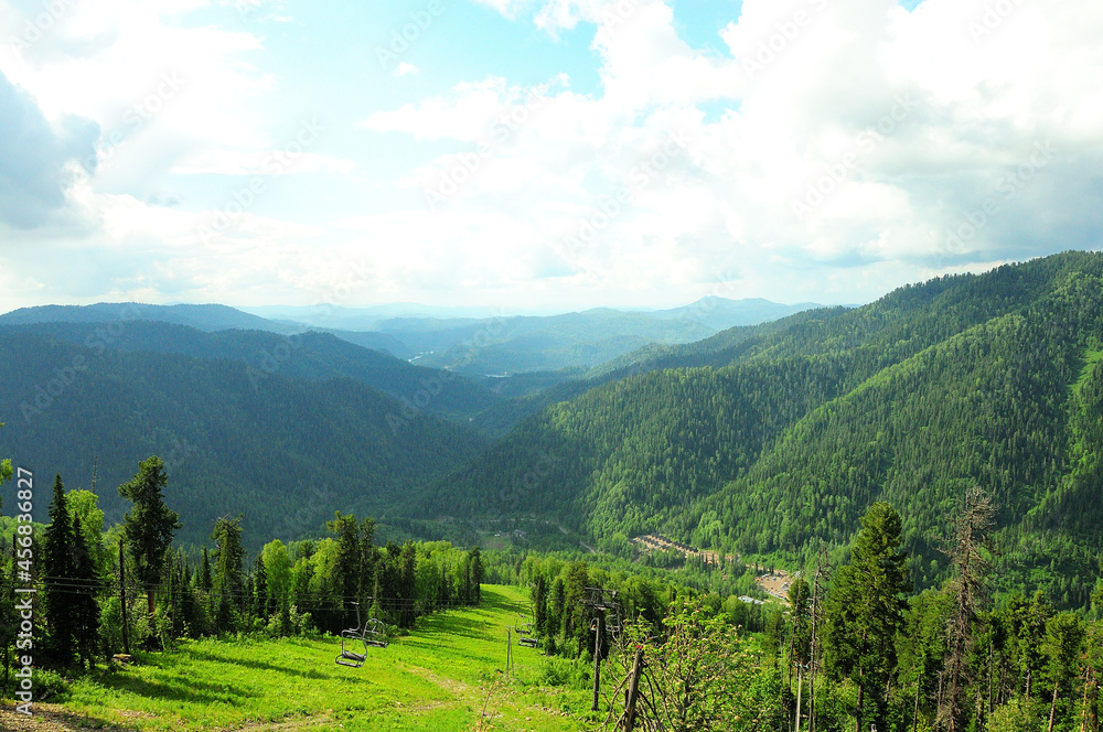 The view from the top of the mountain to the high hills overgrown with forest and the cable car of the chair lift descending into the valley.