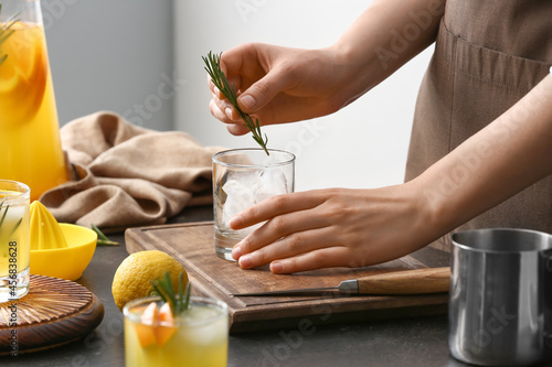 Fotografi Woman making cocktail with rosemary on table in kitchen