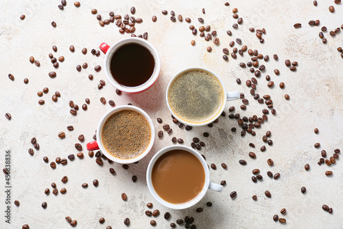 Cups of tasty coffee and beans on light background