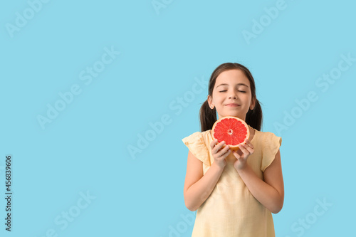Little girl with fresh tasty grapefruit on color background