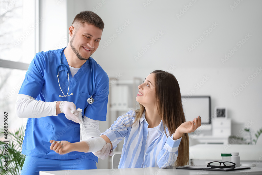 Obraz premium Doctor applying bandage onto arm of young woman in clinic