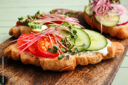 Tasty croissants with vegetables and micro green on color wooden background, closeup