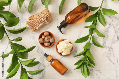 Bowl of shea butter, nuts, bath supplies and plant branches on light background photo