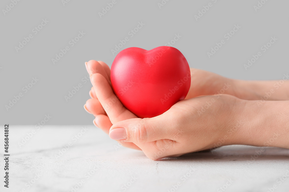 Obraz premium Female hands holding red heart on light background, closeup