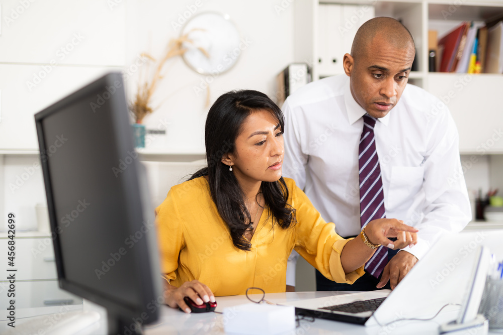 Obraz premium Focused male and female business colleagues looking at laptop screen, discussing new project in office