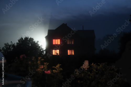 halloween concept. blurred defocused night time scene with hounted house and garden. foggy night, glowing windows and creepy mood