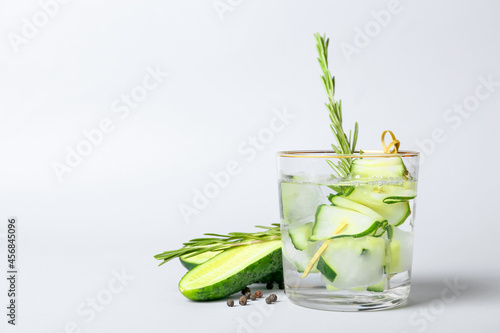 Glass of cold gin tonic and cucumber slices on light background photo