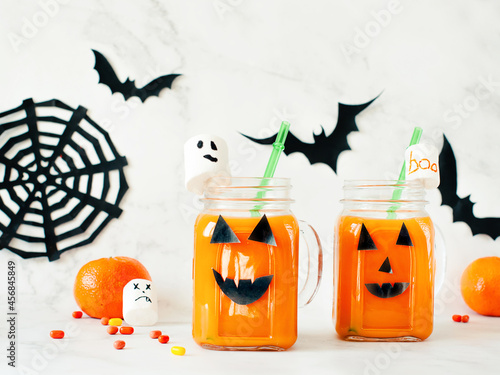 Drink for Halloween. hildren's and party of Halloween treats. Pumpkin orange cocktail in glasses, decorated with creepy faces scary marshmallows on a white marble table. Copy space photo