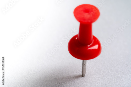 red push pin stuck in white floor. Macro thumbtack top view. white background and copy space
