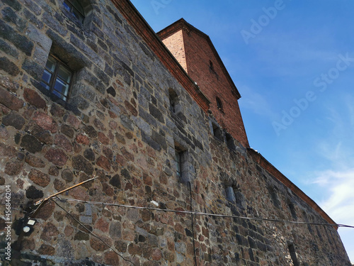 The outer stone wall and the tower of the Vyborg Castle in the city of Vyborg against the blue sky.