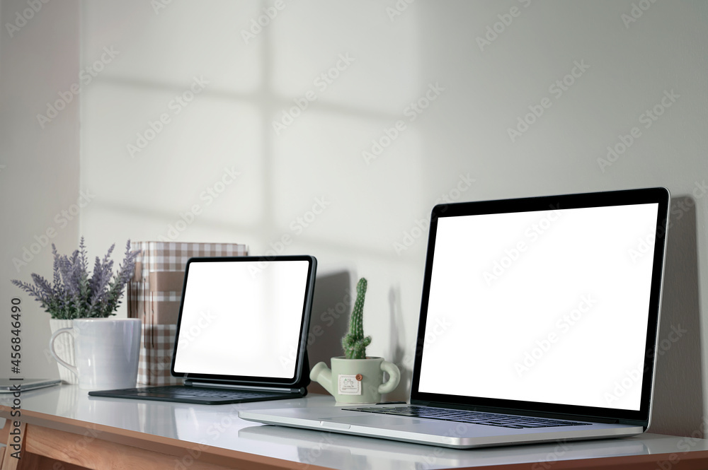 Blank white screen laptop and tablet with magic keyboard on wooden table, home office concept. Blank white screen laptop and tablet with magic keyboard on wooden table, home office concept.